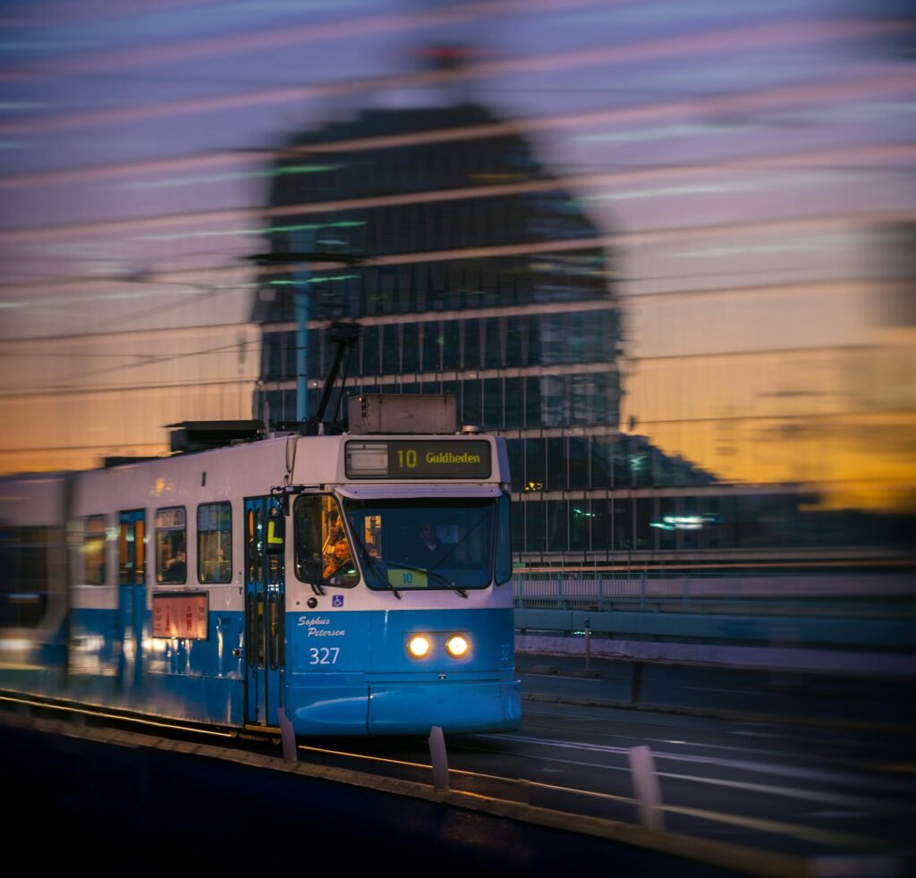A blue tram crosses a bridge in Gothenburg at twilight, reflecting urban lights.