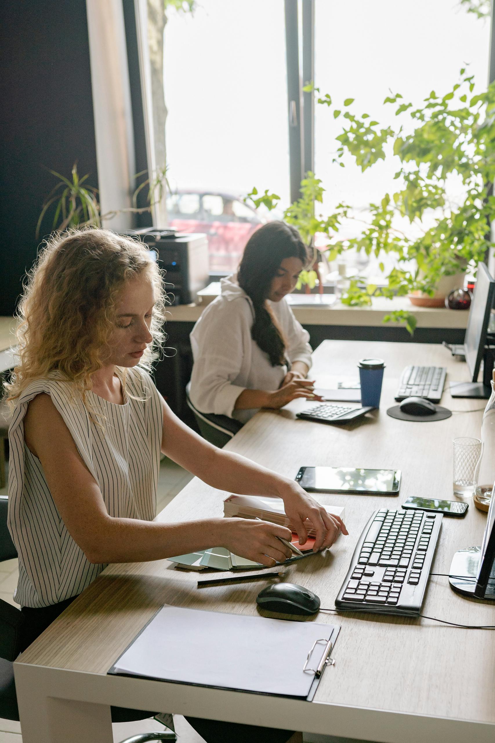 Two women focused on work in a bright, plant-filled office space.